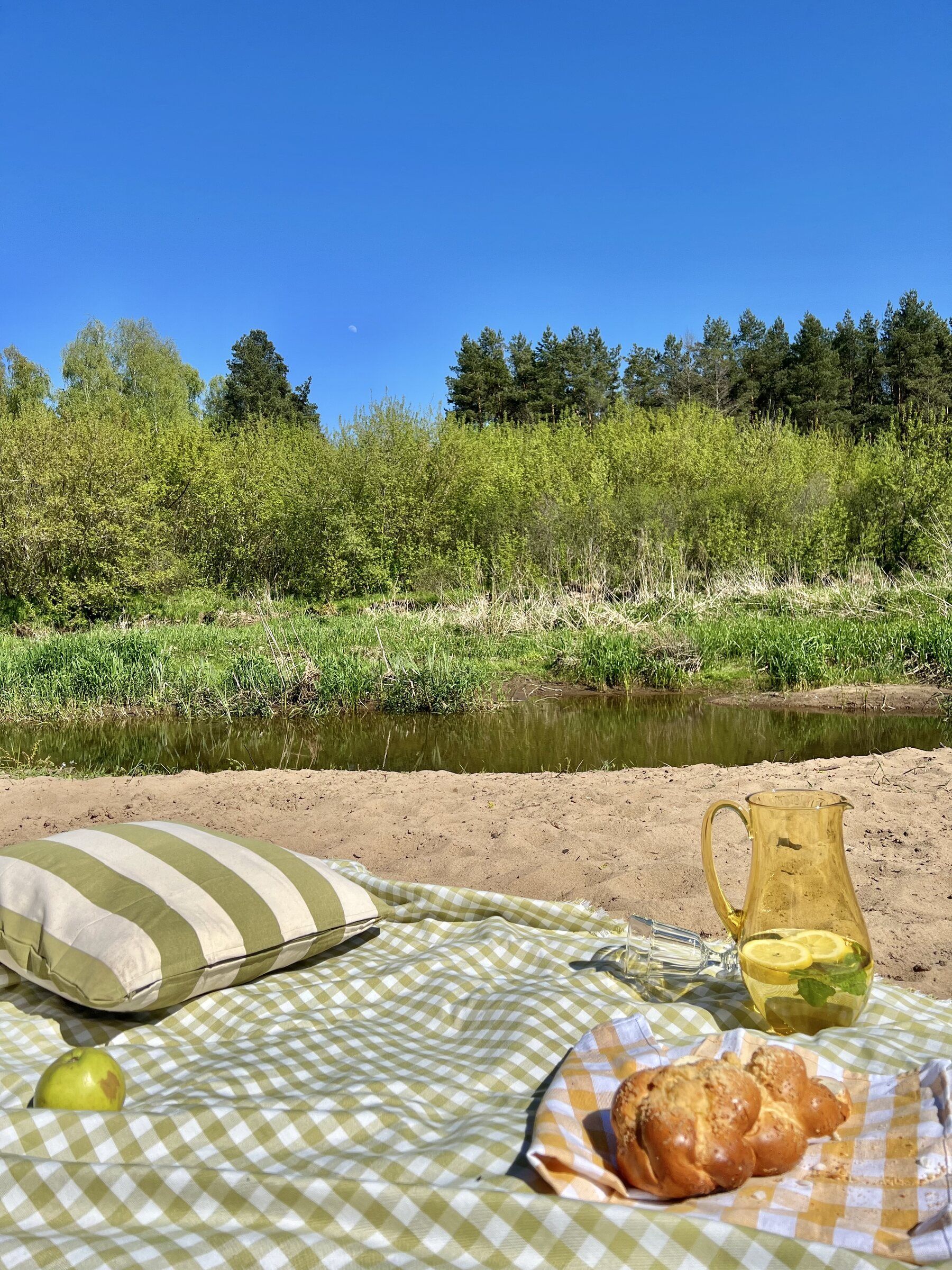 Koc piknikowy z koszykiem pieczywa na piaszczystym brzegu rzeki Liwiec
